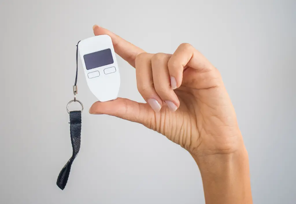 A hand holding up a hardware wallet device.