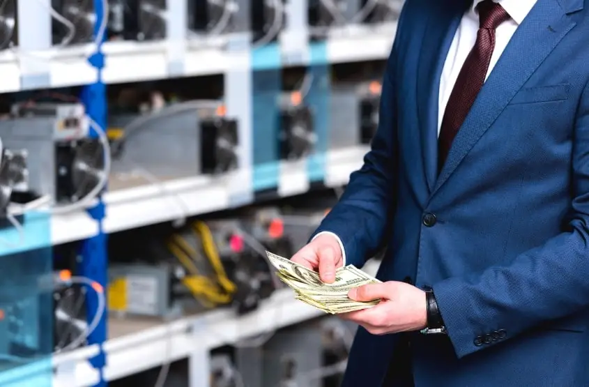 A money with cash standing next to mining rigs